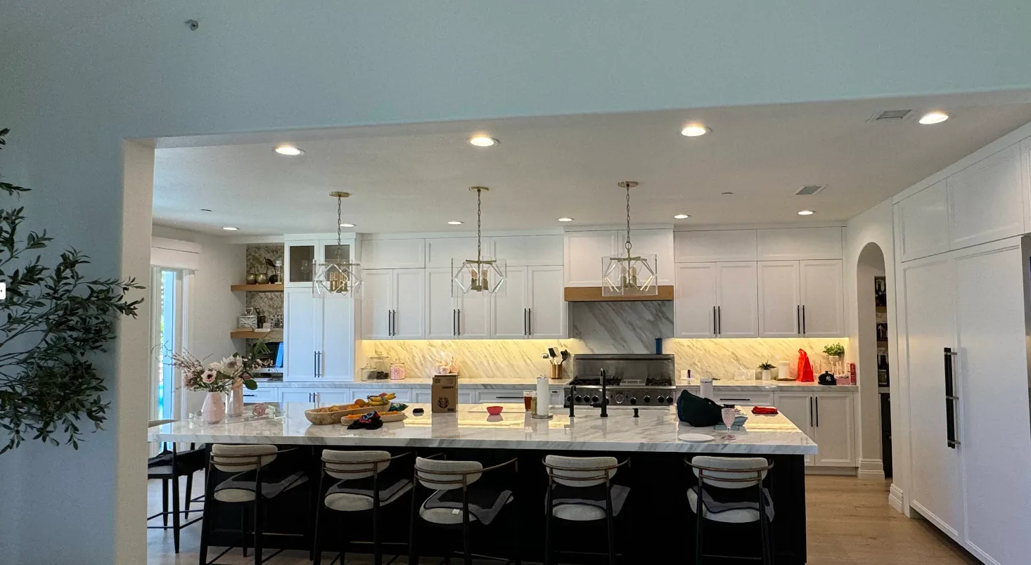 An open-plan kitchen with white cabinetry, marble backsplash and a stone island with seating