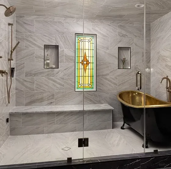 Finished bathroom: large-format grey marble-look tile, glass shower enclosure, built-in bench, recessed niches and a freestanding tub