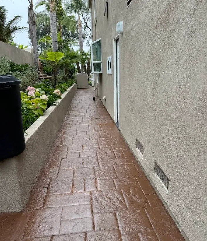 A finished stamped concrete side walkway coated in terracotta, against a stucco wall